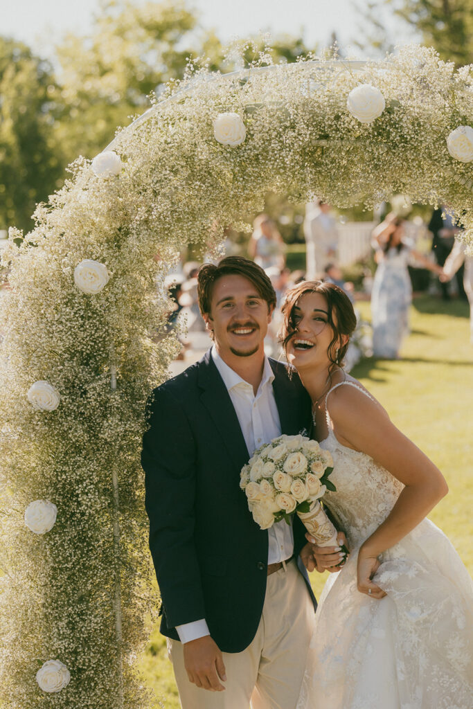 Bride and groom at ceremony laughing under flower arch