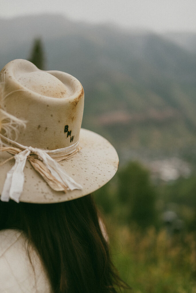 A close up of a white bridal hat with raindrops and stamped initials in front of a gondola