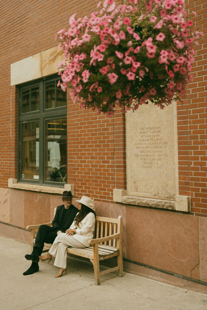 A couple on their elopement day in front of a library sitting on a bench