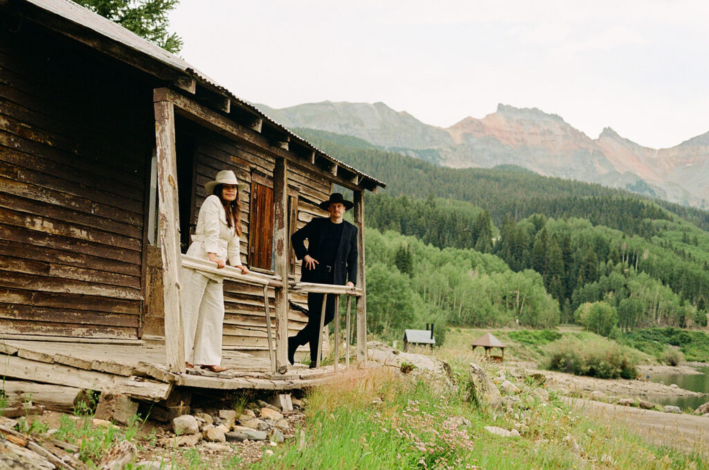 A couple on their elopement day in Telluride, CO posing in an old wooden cabin with mountains in the background