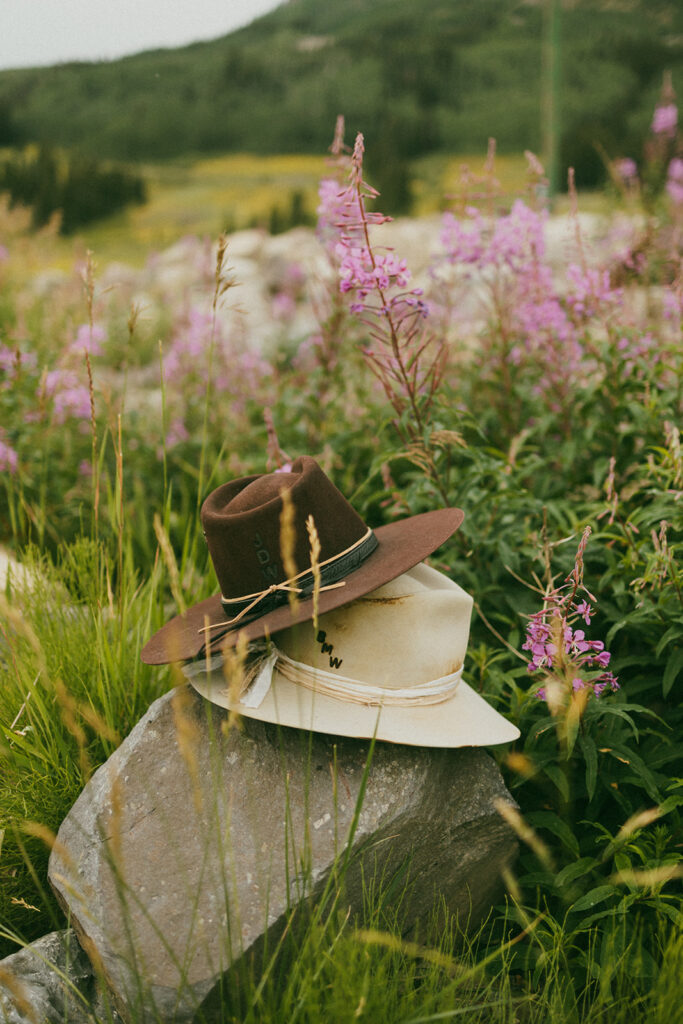 A pair of hats in the middle of a wildflower field with stamped initials. 