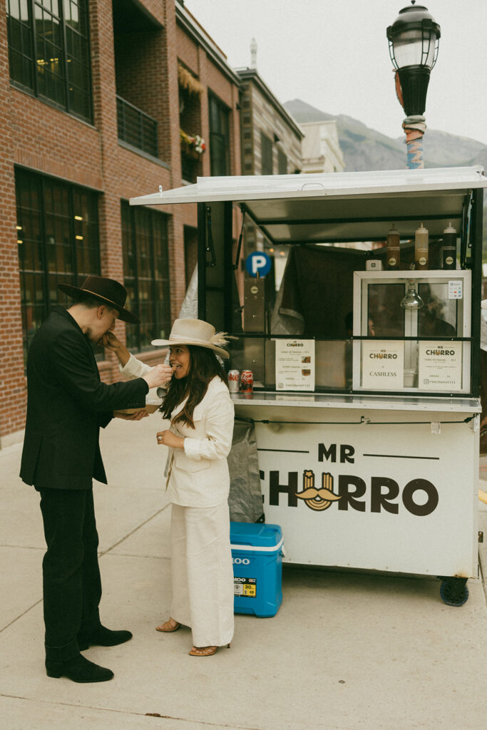 A couple on their elopement day eating a churro from a street booth