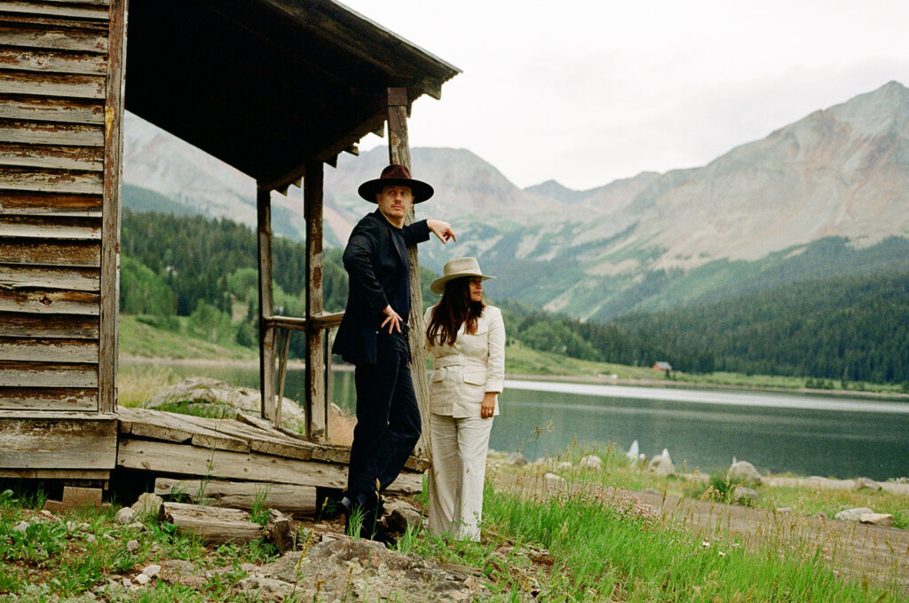 A couple on their elopement day in Telluride, CO posing in an old wooden cabin with mountains in the background