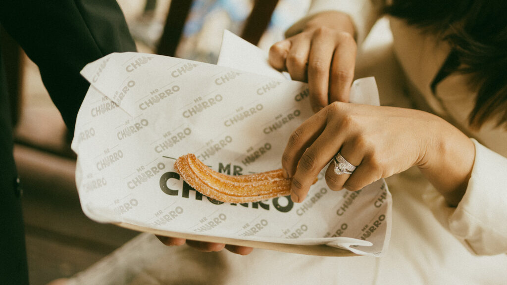 A couple on their elopement day eating a churro from a street booth